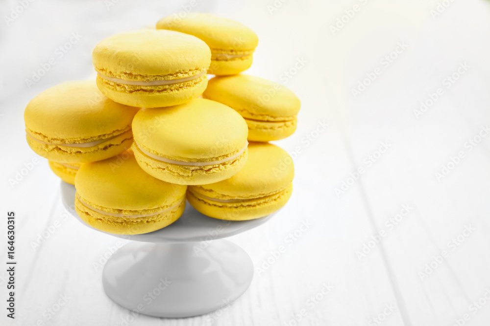 Stand with tasty lemon macarons on white wooden table, closeup