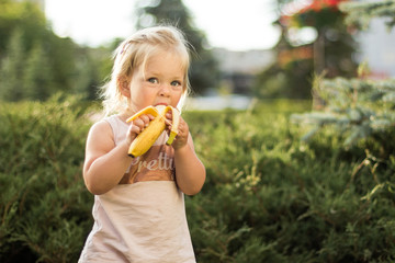 A little girl is eating a banana in a park outside. Lunch and healthy lifestyle.