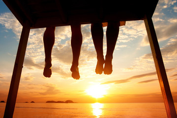 happiness concept, silhouette of feet of couple sitting on the pier at sunset beach