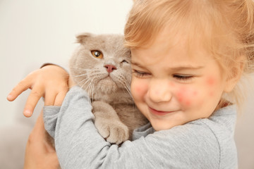 Closeup of adorable little girl embracing cute cat in the room