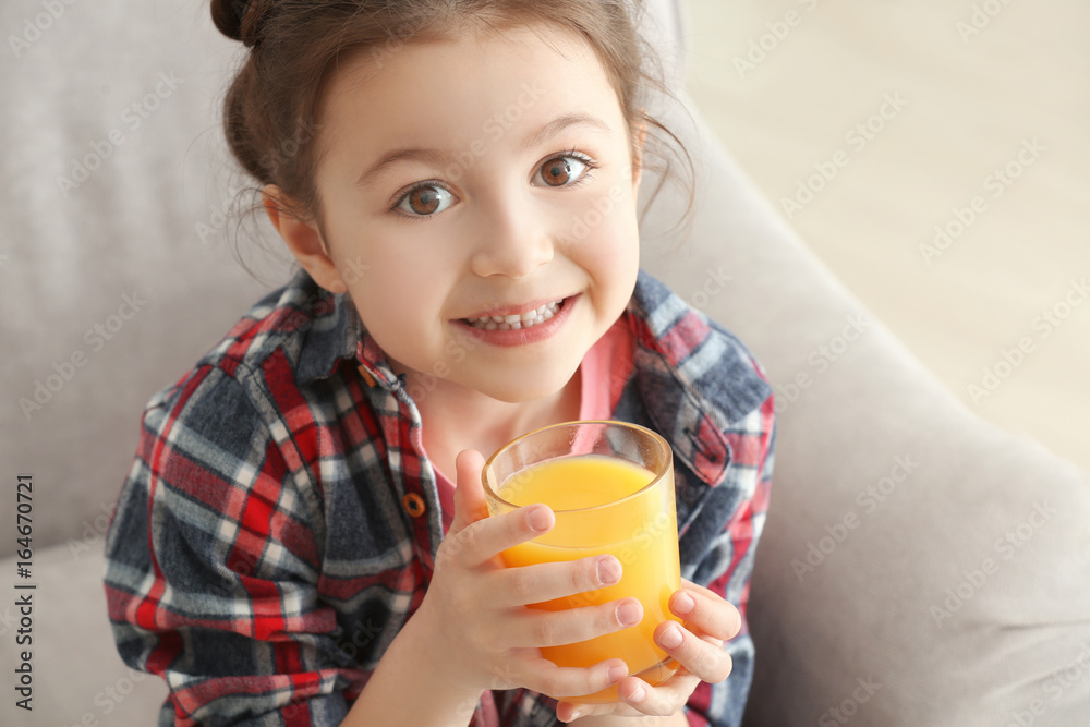 Cute little girl drinking juice while sitting on sofa at home, closeup
