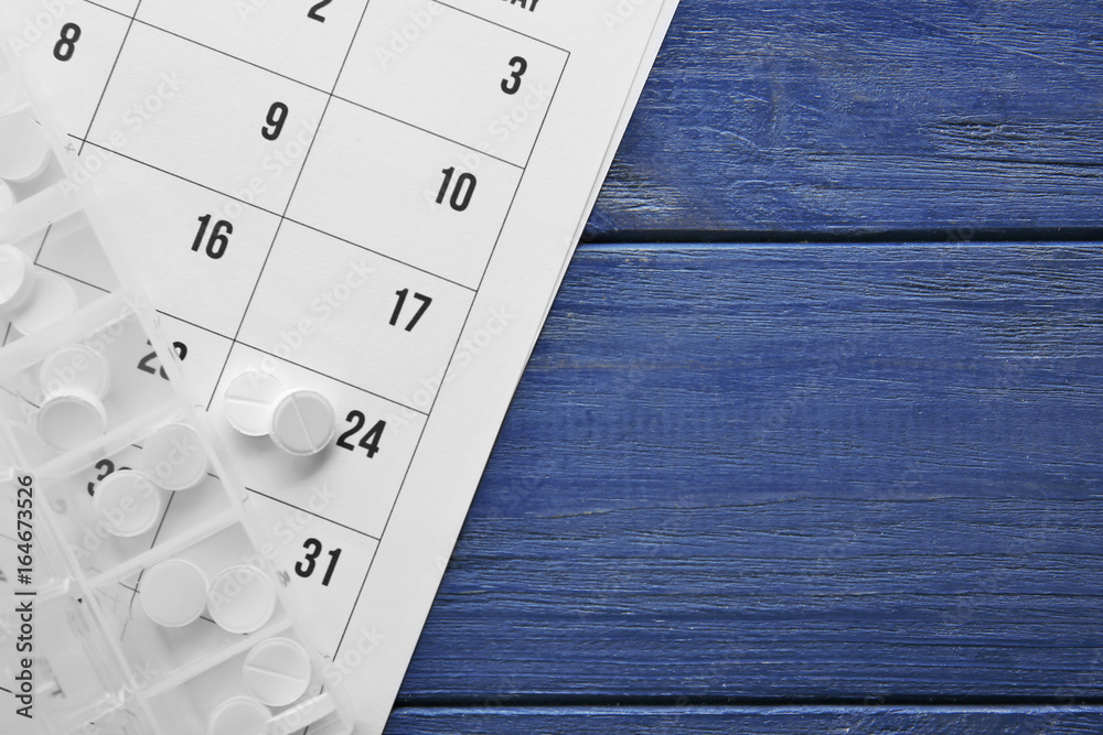 Plastic container with pills and paper calendar on wooden table