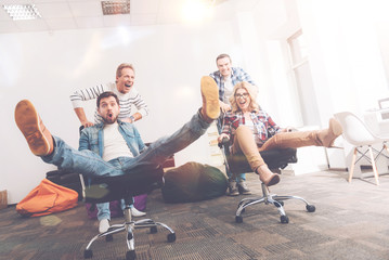 Positive colleagues riding in office chairs