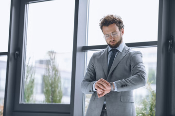 Wall Mural - portrait of handsome businessman in eyeglasses looking at watch to check time