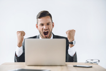 Wall Mural - portrait of excited businessman looking at laptop screen at workplace isolated on white