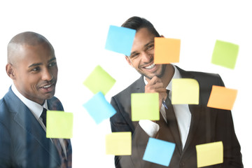 Wall Mural - multicultural smiling businessmen looking at sticky notes isolated on white