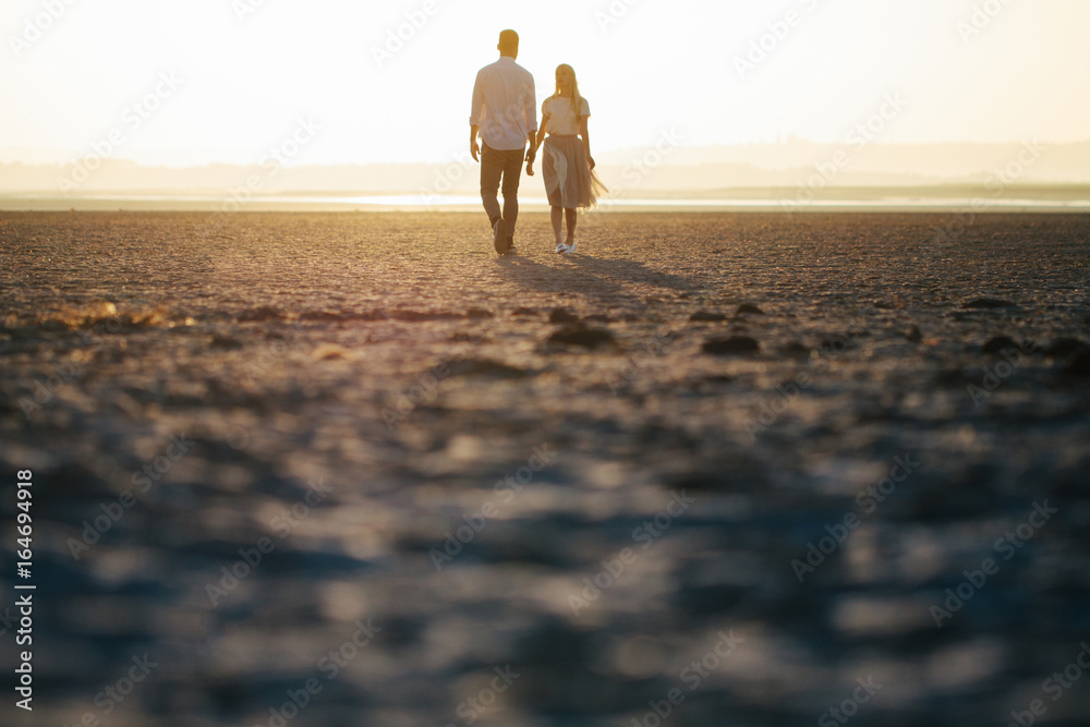 Couple in love walking on the beach and looking at each other - obrazy, fototapety, plakaty 
