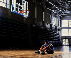 Wall Mural - Basketball player sits on a field under the hoop.