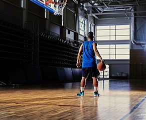 Wall Mural - Basketball player holds a ball over the hoop in a game hall.