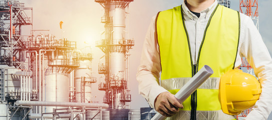 engineering man standing with white safety helmet against oil refinery in petrochemical Aerial view oil refinery night during twilight,Industrial zone,Energy power station background.