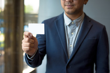 Wall Mural - Man holding white business card,Man wearing blue shirt and showing blank white business card. Blurred background. Horizontal mockup, Smart asian business Person Professional Occupation cheerful