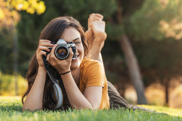 Smiling young woman using a camera to take photo at the park.