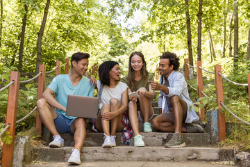 Canvas Print - Multiethnic friends students outdoors using mobile phone and laptop