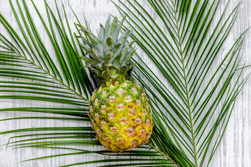  Pineapple and palm branch on wooden desk background top view