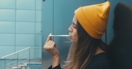 Wall Mural - CU Outdoor portrait of young attractive female in stylish outfit chewing gum. 4K UHD RAW edited footage