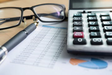 financial charts on the table with laptop, calculator, pen and glasses business concept