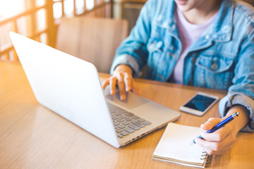 woman's hand using laptop and writing in notepad