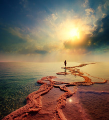 Fototapete - Woman walking on Dead Sea salt shore towards the sun