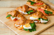 Croissant Sandwiches Served On Wooden Board. Croissants With Egg, Melted Cheese, Parsley, Chicken Ham, Smoked Salmon