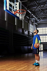 Wall Mural - Basketball player holds a ball over the hoop in a game hall.