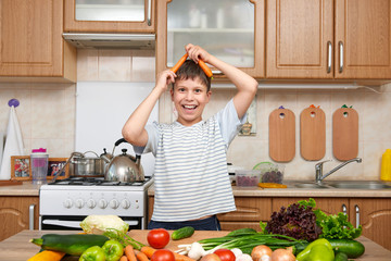 Child boy having fun with carrot. Home kitchen interior with fruits and vegetables. Healthy food concept