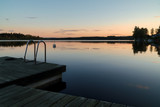 Fototapeta Pomosty - Calm summer evening sunset, jetty with ladder in reflection lake