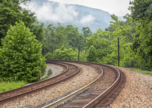 Curving Double Railroad Tracks Through Foggy Mountains