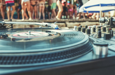 Summer beach party - turntable closeup and blurred dancing crowd of people