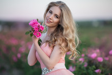 Beautiful Pretty Woman Is Wearing Fashion Dress Posing Near Pink Roses In A Garden