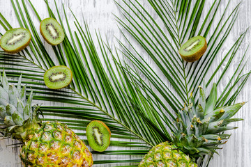  Summer exotic fruits. Kiwi, pineapple and palm branch on wooden background top view