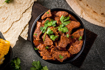 Mexican and American traditional food. Stew beef with tomatoes, spices, pepper - Chile Colorado. With tortillas.  Copy space, on black stone table