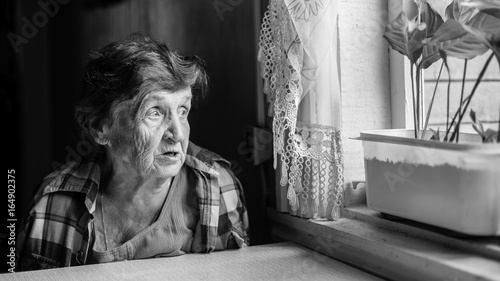Elderly woman grieves near the window genre photography in black and white Elderly woman grieves near the window genre photography in black and white