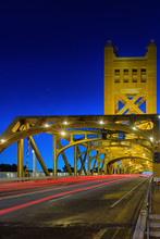 A Brightly Lit Yellow Lift Style Bridge At Dusk With Taillight Flairs Shown As A Car Passes