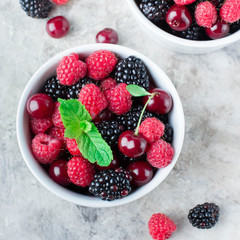 Close up of Summer fresh berries in white bowl on gray concrete table background. Top view with copy space. Vegetarian food - raspberry, blackberry and cherry