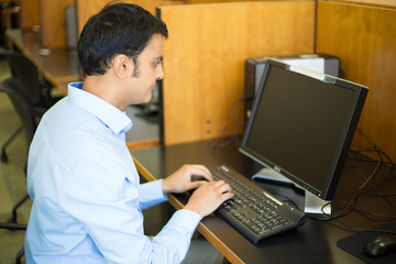 Sticker - Closeup portrait, young handsome man in blue shirt typing away, browsing digital computer, isolated background of indoors library cubicle background