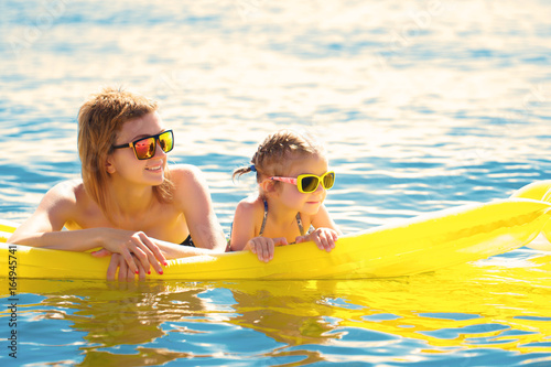 Fotografie, Obraz Mother and daughter in sunglasses floating on airbed together.
