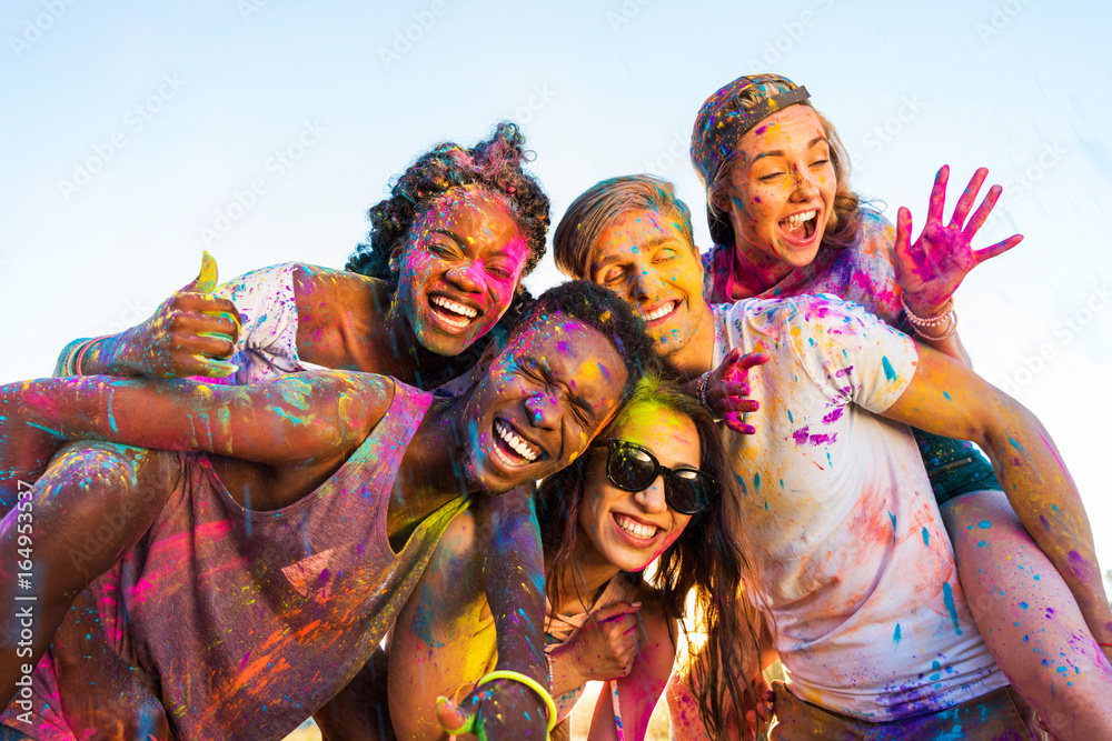 happy young multiethnic friends with colorful paint on clothes having fun together at holi festival - obrazy, fototapety, plakaty 