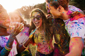 cheerful young multiethnic friends with colorful paint on clothes and bodies having fun together at 