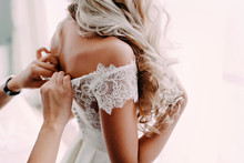 Gorgeous, Blonde Bride In White Luxury Dress Is Getting Ready For Wedding. Morning Preparations. Woman Putting On Dress.