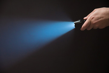 Male hand holding a led flashlight with a narrow blue beam on a black background, leaving the right side of the frame