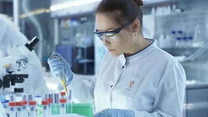 Wall Mural - Female Research Scientist Uses Micropipette Filling Test Tubes in a Big Modern Laboratory. In the Background Scientists are Working. Shot on RED EPIC-W 8K Helium Cinema Camera.