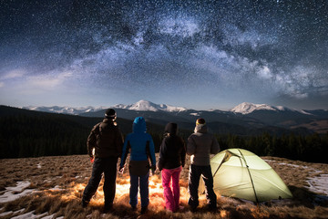 silhouette of four people standing together beside camp and tent under beautiful night sky full of s