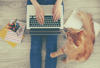 Woman typing on laptop and sitting on floor with fluffy cat