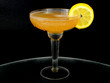 A whisky sour in a coupe glass with a lemon wagon wheel garnish on a dark background