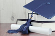 A blue graduation cap resting on two books with a diploma tied with blue ribbon on a wooden background. Copy space. White vignette added