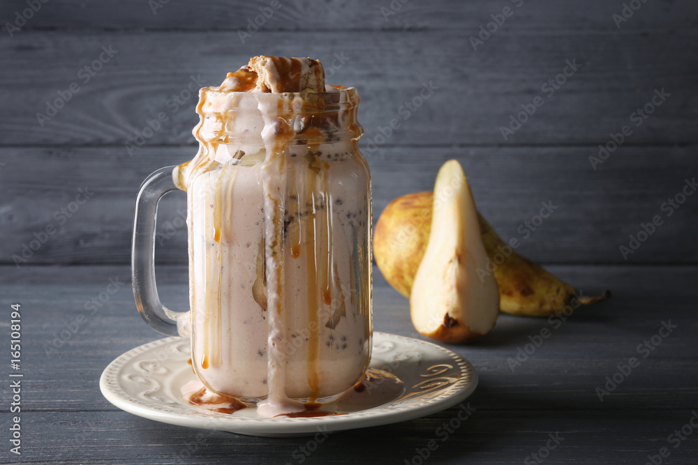 Delicious yogurt parfait in jar and pear on table