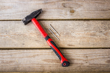 A hammer with a red handle and two nails on a background of light unplaned boards