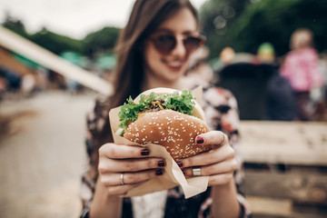 Wall Mural - tasty burger. stylish hipster woman holding juicy hamburger in hands close up. boho girl with hamburger at street food festival. summertime. summer vacation picnic. space for text