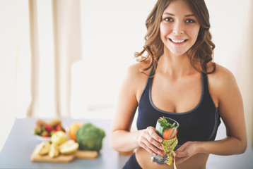 Woman holding a drinking glass full of fresh fruit salad with a tape measure around the glass.