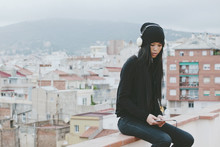 Young Chinese Woman Listening Music On Tablet Sitting On Rooftop. Winter Scene.